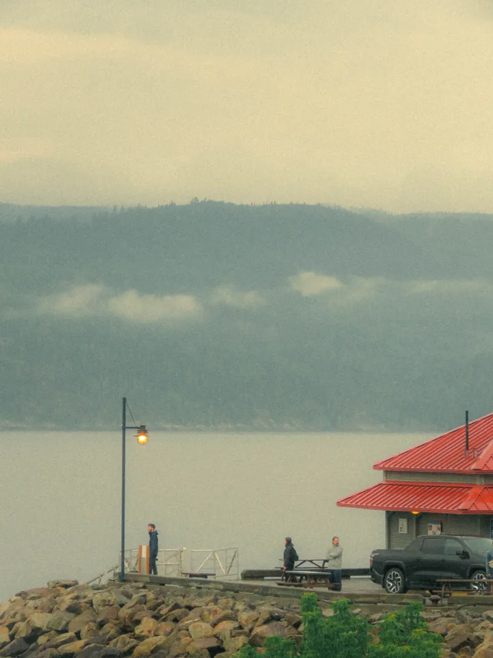 A glowing lamp and red-roofed shelter on a misty shoreline