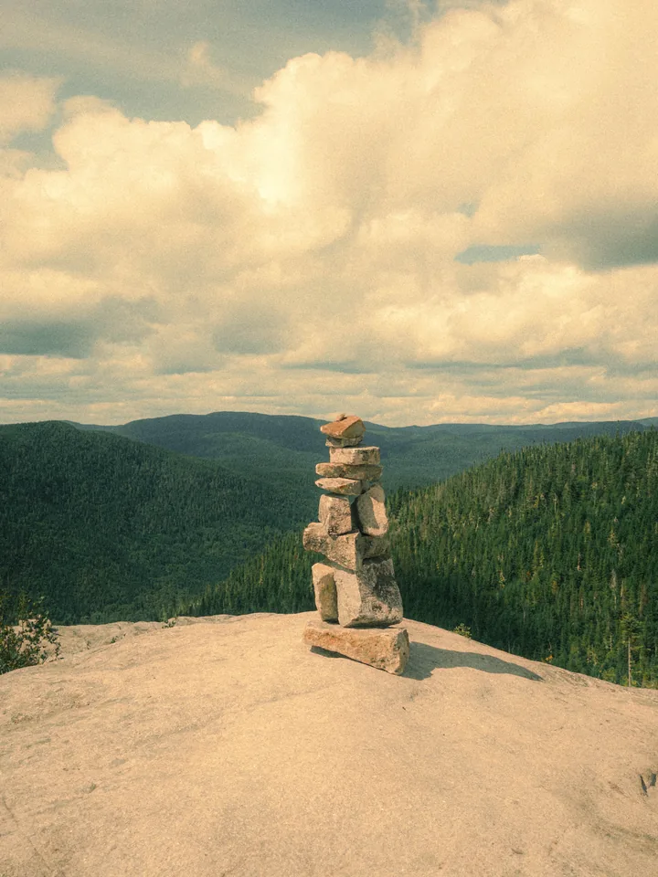 A stone cairn on a sunny summit beneath large clouds