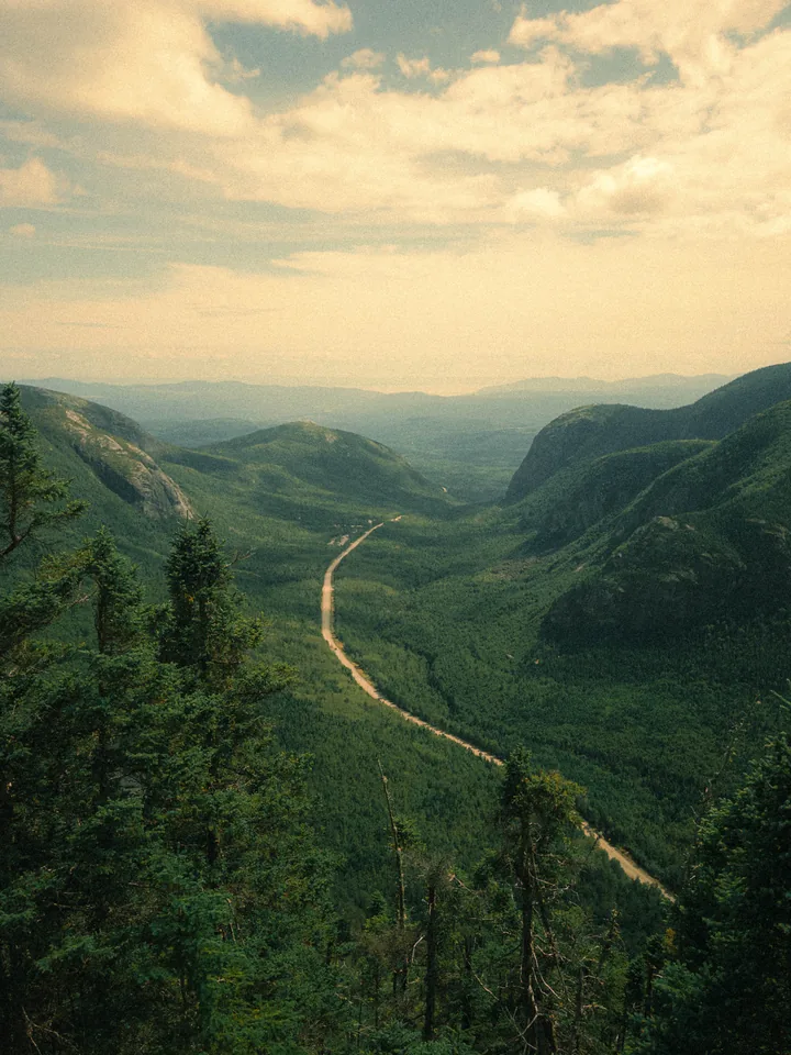 A distant road threading through a deep green mountain valley