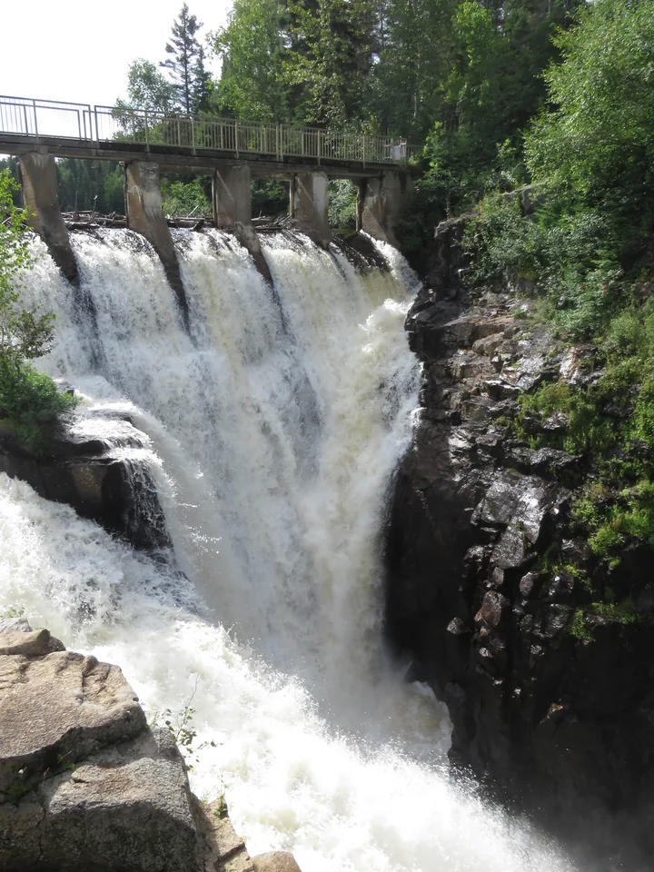A powerful waterfall beneath a footbridge on a sunny day